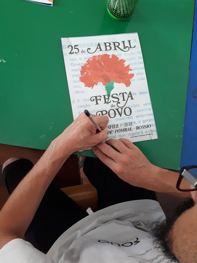 Adulto a desenhar um cravo num cartaz alusivo ao 25 de Abril