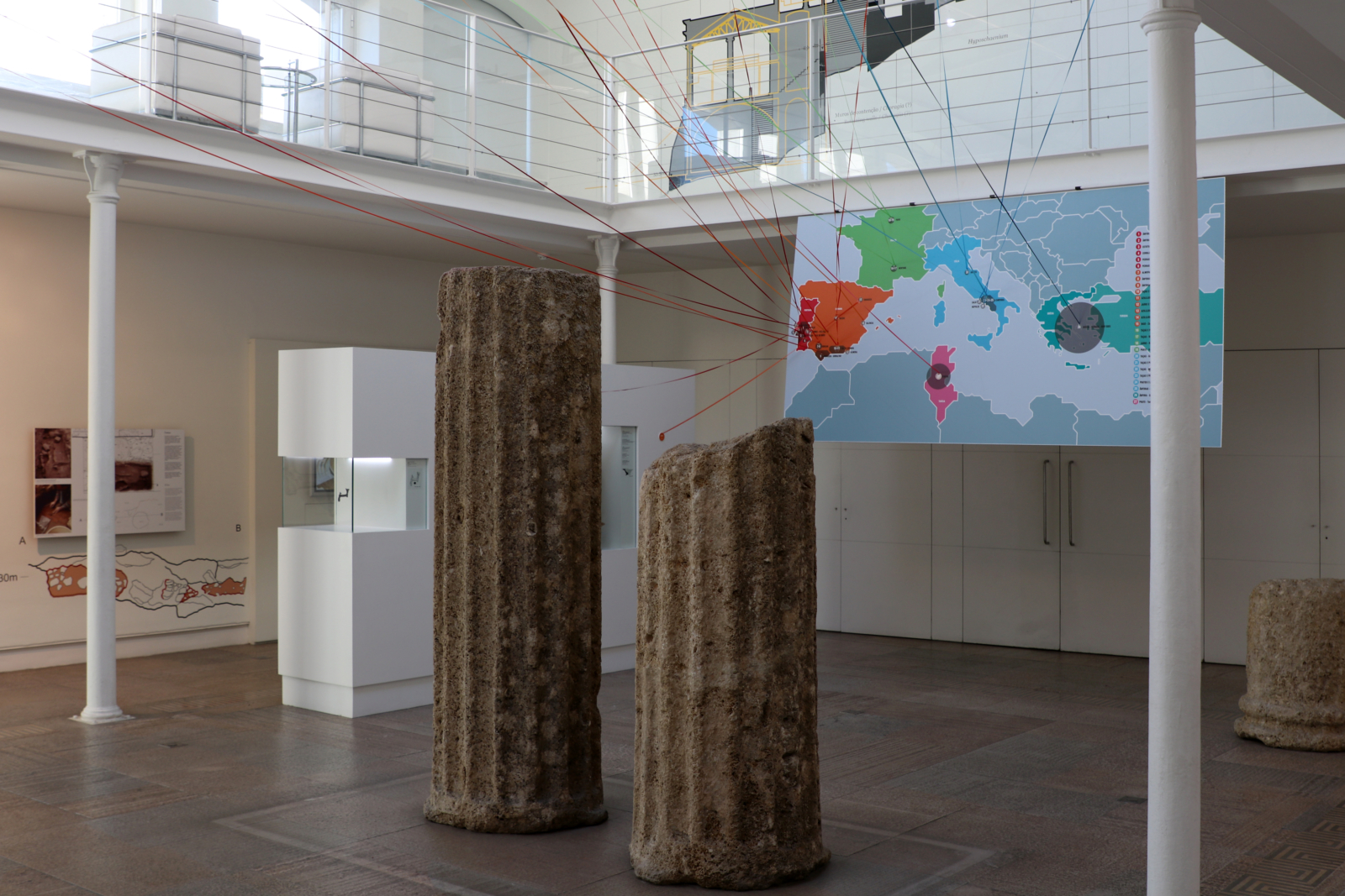 Espaço expositivo, com duas colunas romanas partidas, e um mapa do mundo