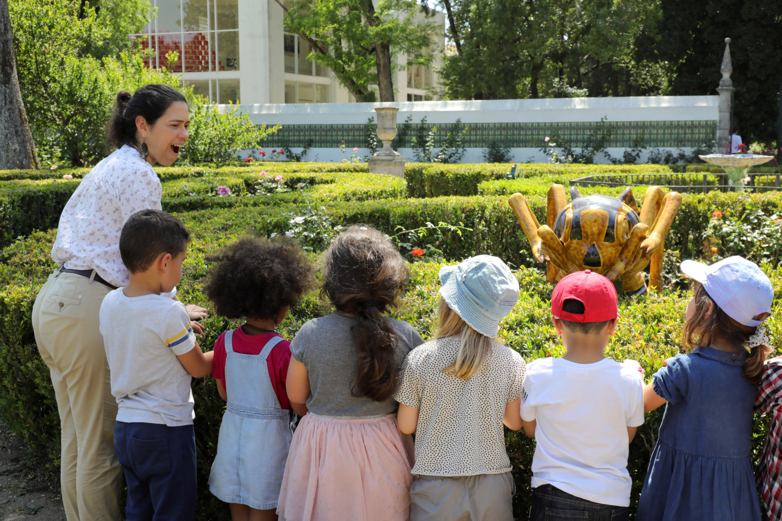 Num jardim, um grupo de crianças observa as plantas e coloca questões a um adulto.